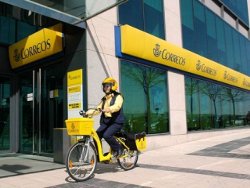 Empleada de Correos en bicicleta ante una oficina de Correos